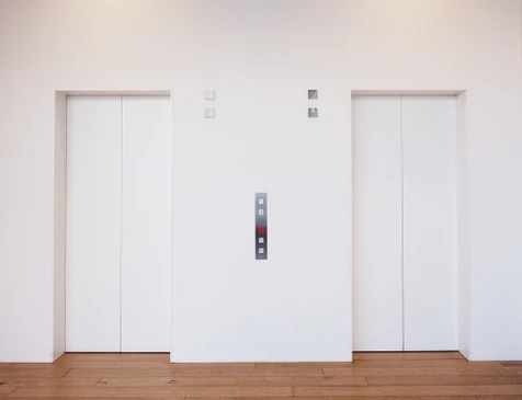 Hall d'entrée moderne avec deux ascenseurs fermés aux portes blanches et encadrements métalliques