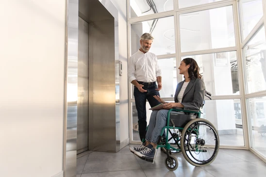 Scène extérieure urbaine montrant une personne en fauteuil roulant utilisant une rampe d'accès pour monter dans un véhicule utilitaire orange adapté au transport de personnes à mobilité réduite